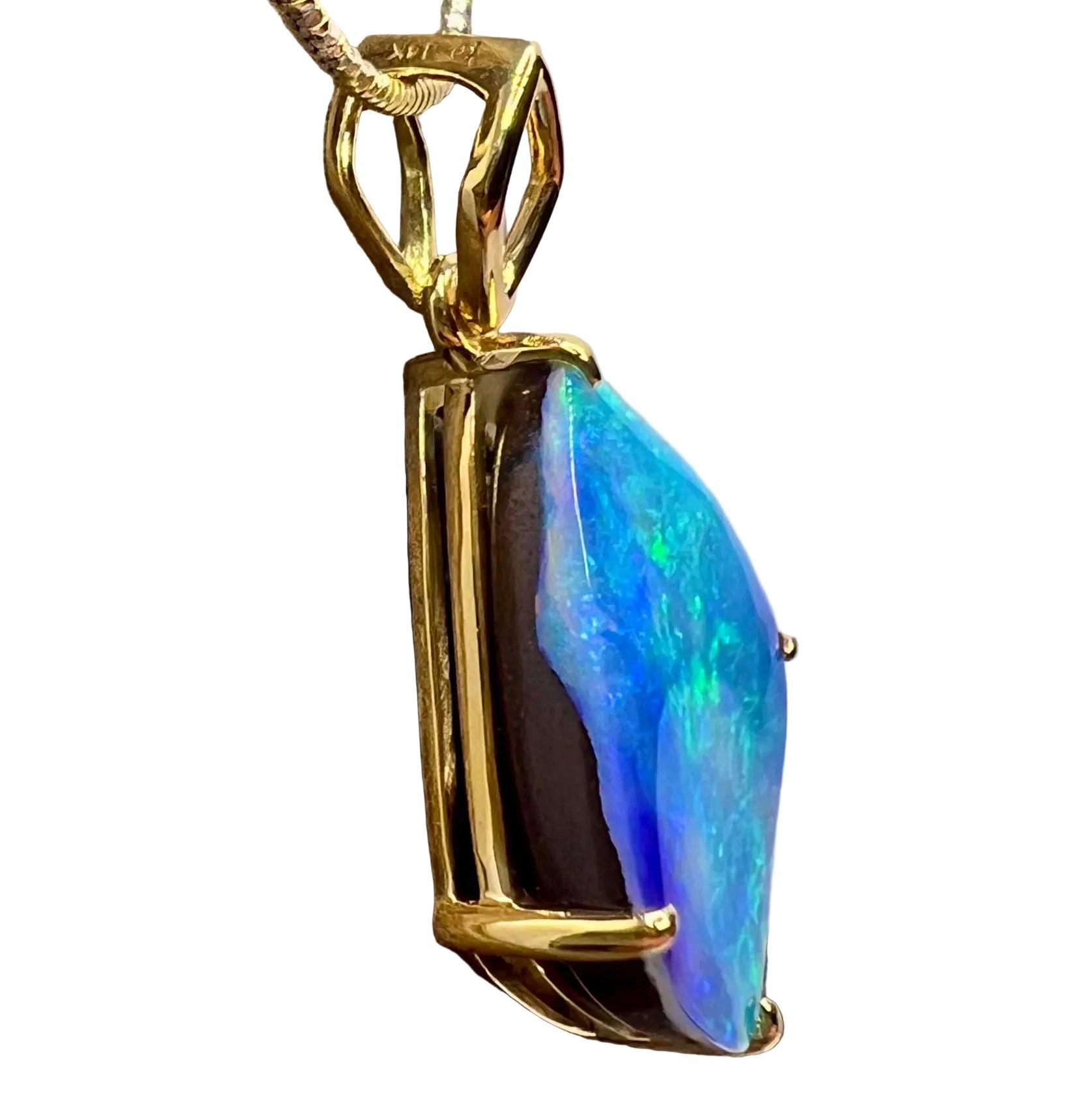 Pale sky blue to ocean blue Australian Boulder Opal cut in a diamond shape with a four claw setting and an open diamond shaped bale hanging above the stone. Set in 18K solid yellow gold. Some shimmering green colours flash across the face of the blue opal. The opal's colouring and patterns are reminscent of a shimmering aqua blue water reflecting in sunlight.