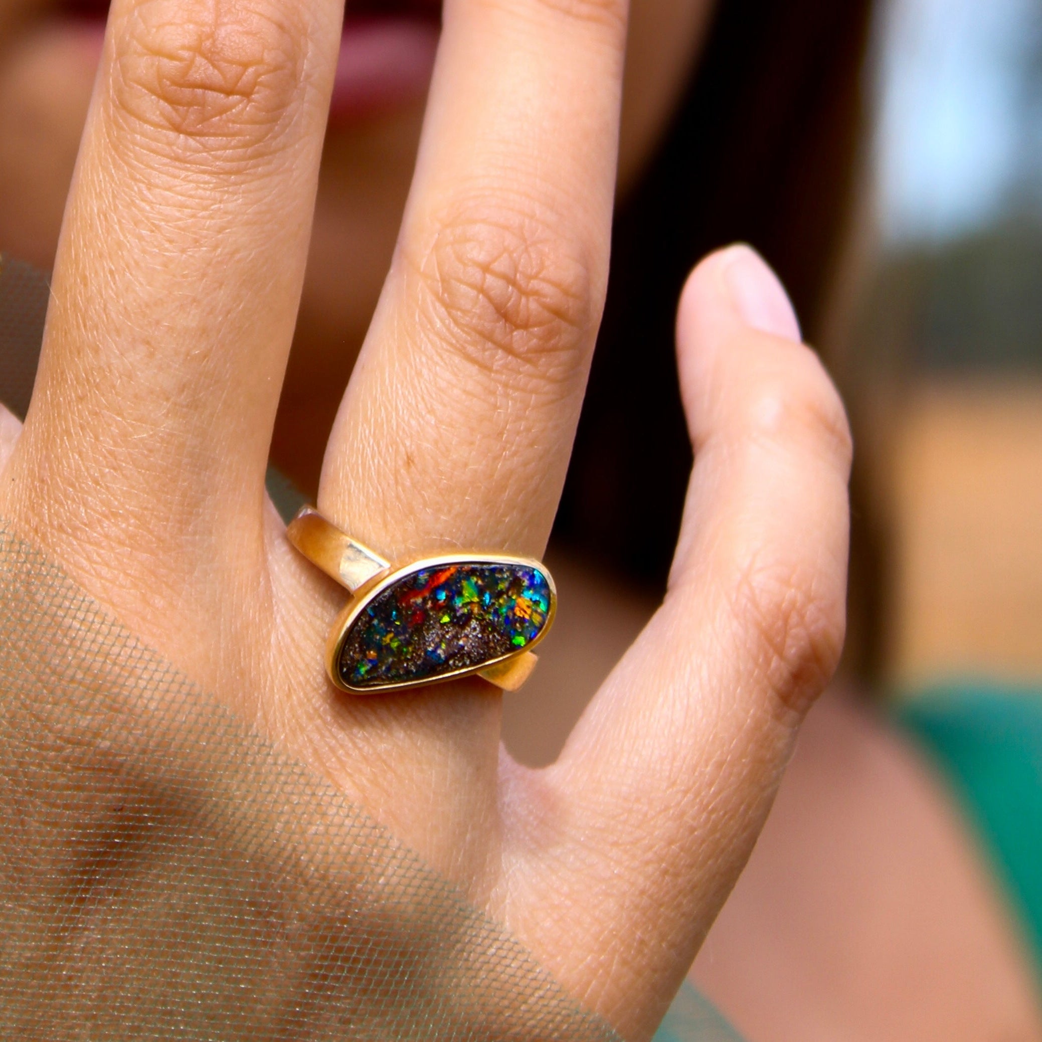 Close-up of a hand wearing an opal ring with a blurred background
