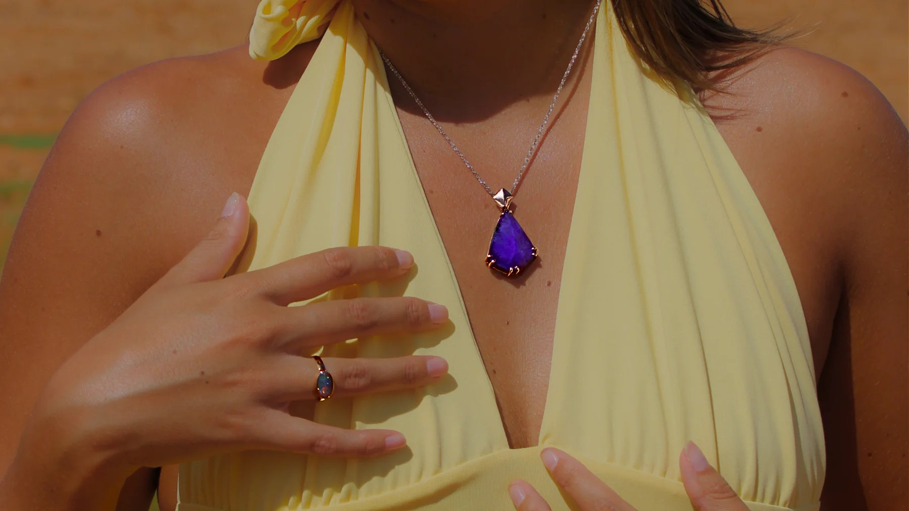 Woman wearing a yellow halter top with a purple teardrop necklace.