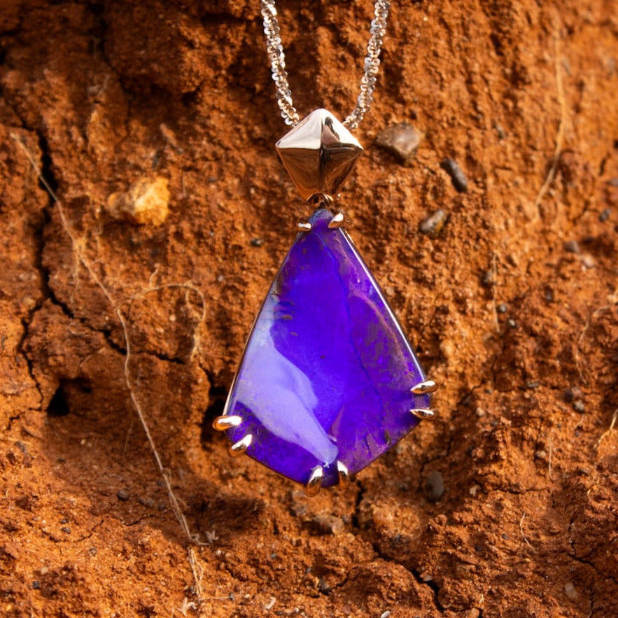Purple teardrop pendant on a chain against a brown textured background