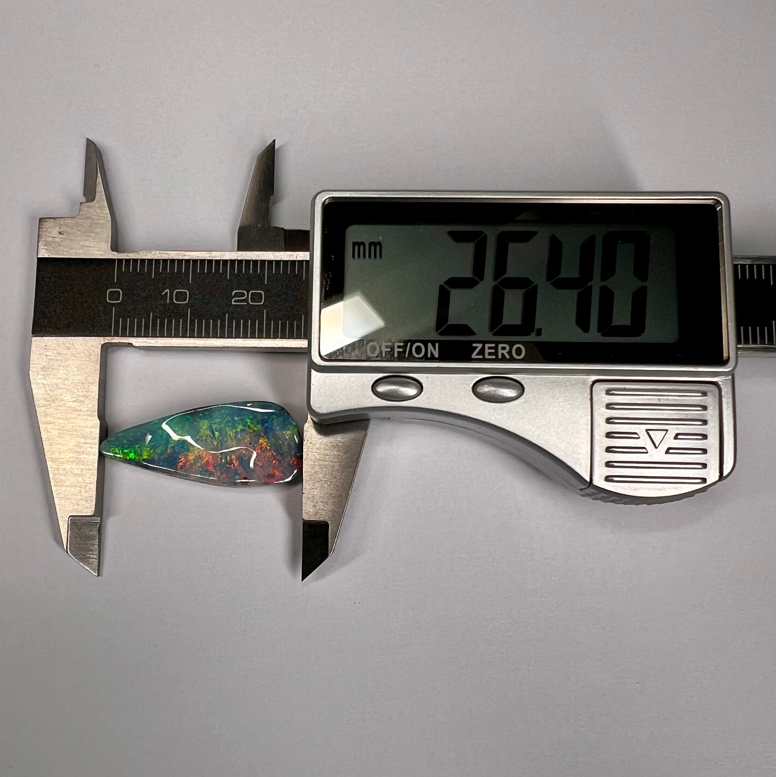 Digital caliper measuring an opal stone on a gray background