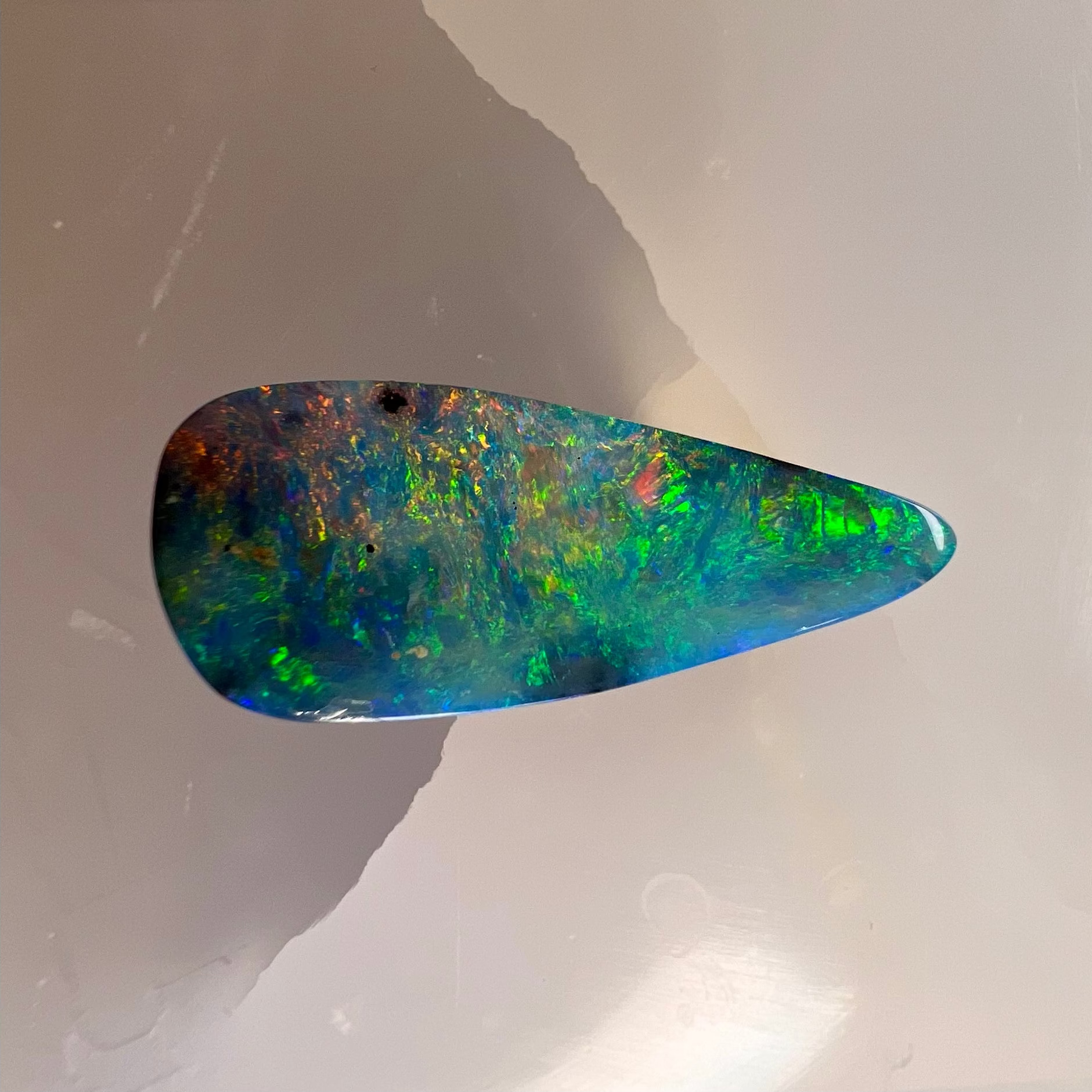 Teardrop-shaped opal stone on a reflective surface