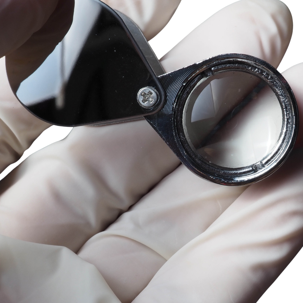 Close-up of a hand wearing a glove holding a magnifying glass.