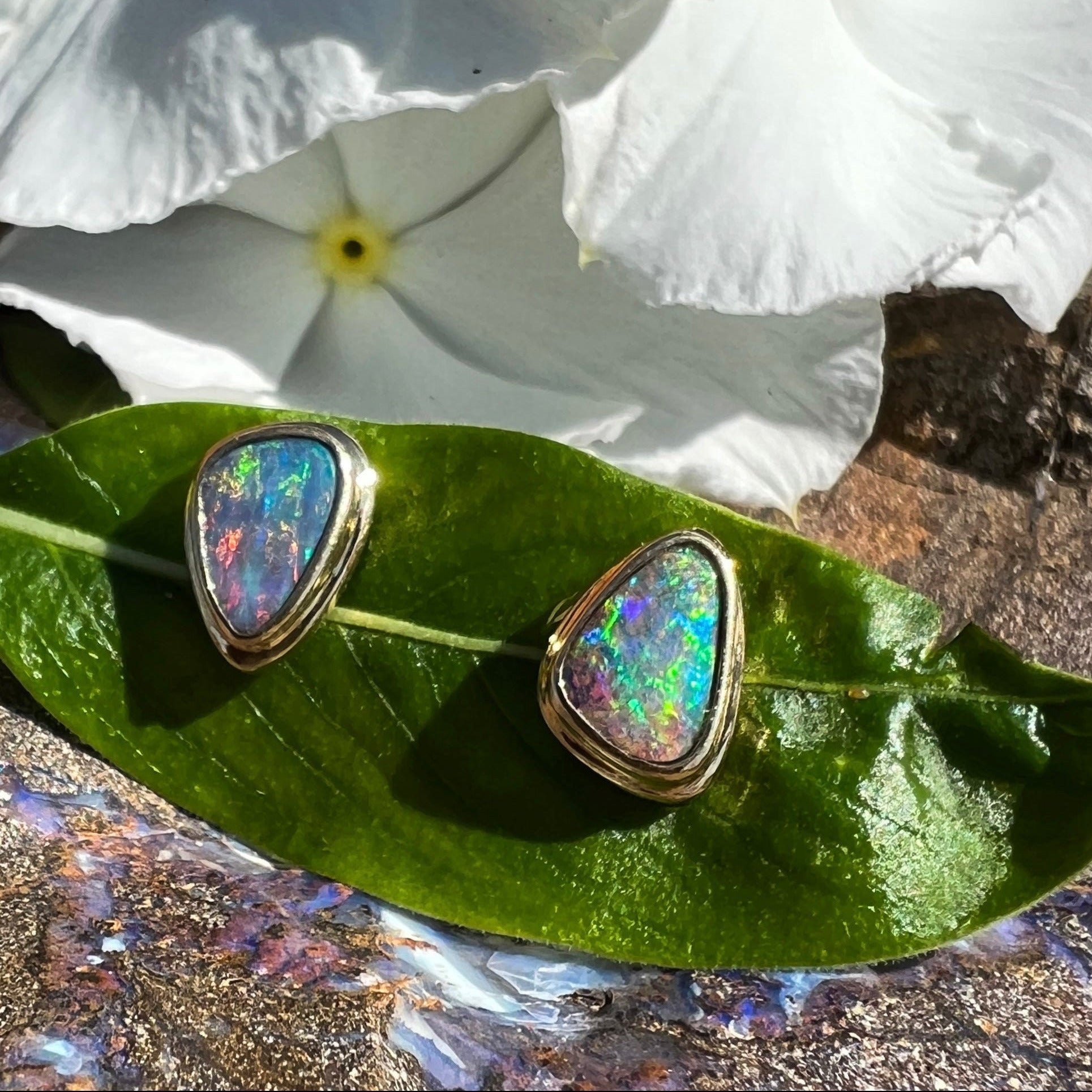 Opal earrings on a green leaf with white flowers in the background