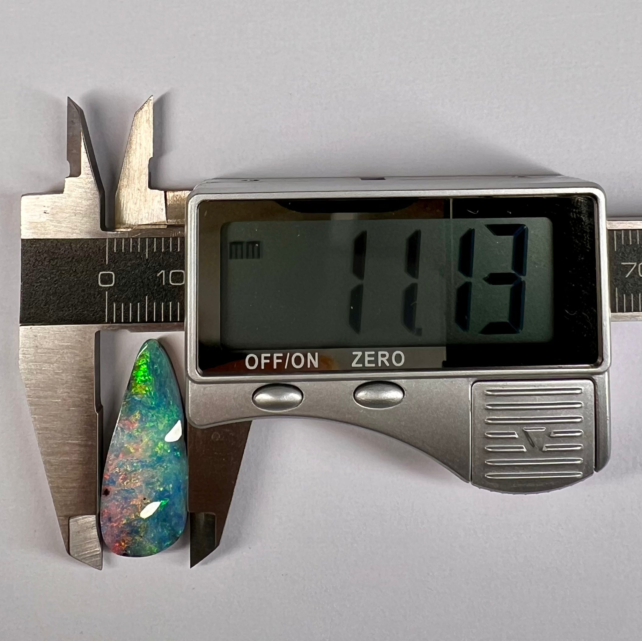 Digital caliper measuring a colorful opal stone against a gray background