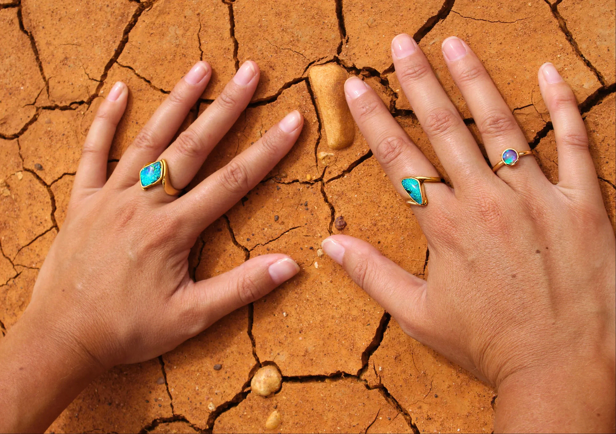Two hands with blue opal rings on cracked red dirt earth