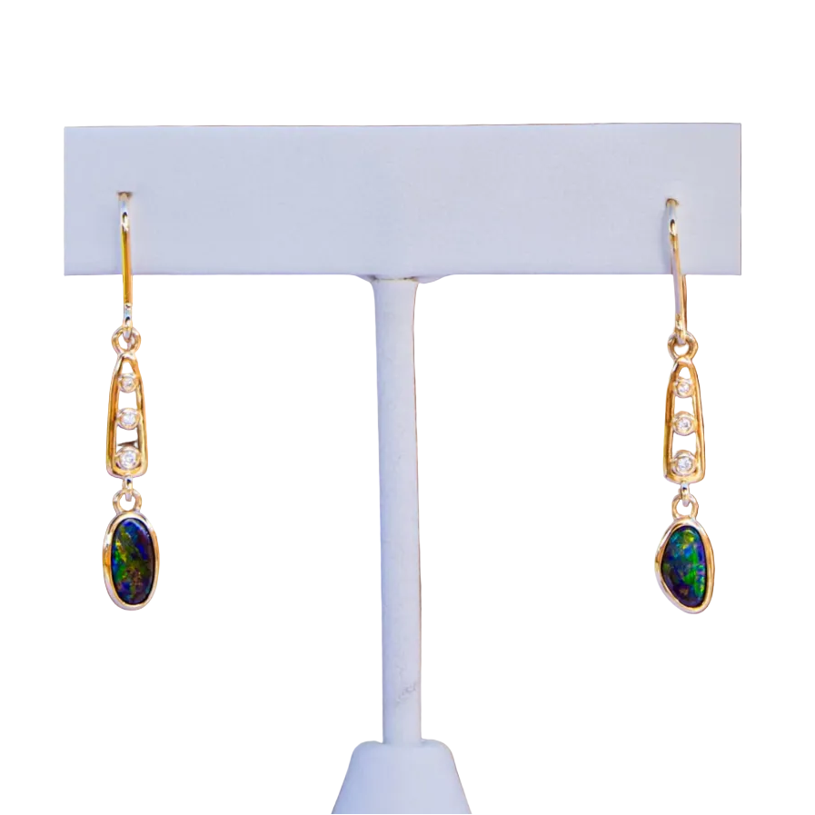 Gold earrings with gemstones on a white stand against a white background