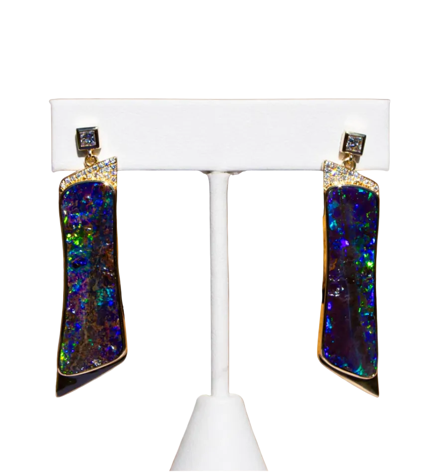 Multicolored opal earrings on a white stand against a brown background